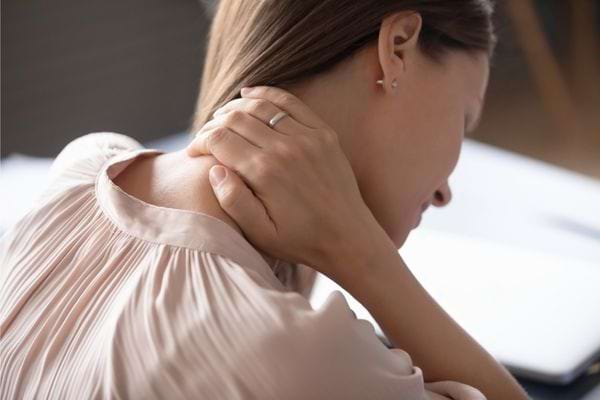 Femme se tenant la nuque avec la main, ressentant une douleur musculaire.