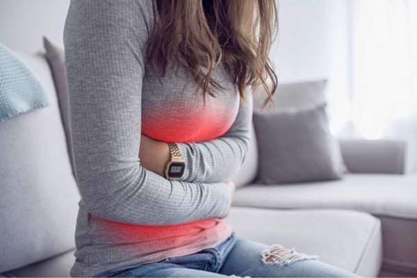 Une femme assise se tient le ventre avec une zone rouge visible de douleur.