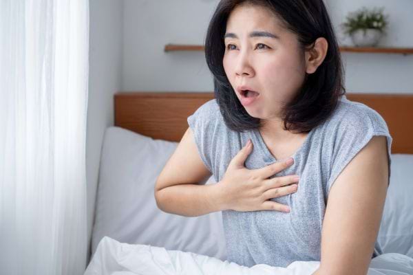 Une femme assise dans son lit, main sur la poitrine, paraît suffoquer.