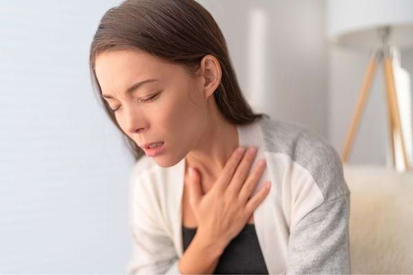 Femme jeune tenant sa poitrine, semblant souffrir d’une douleur ou d’un essoufflement.