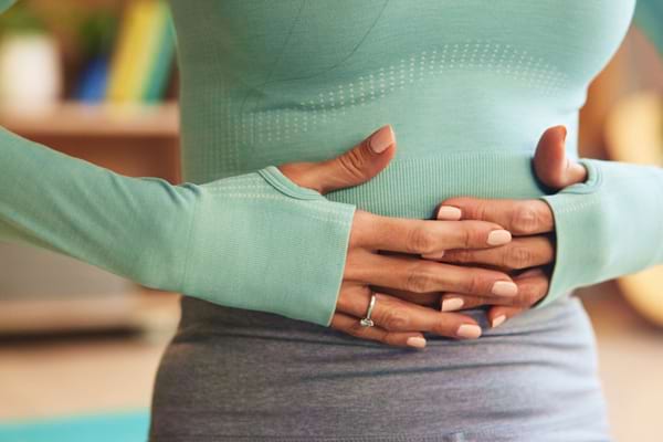 Une femme se tient le ventre avec les deux mains, exprimant une douleur abdominale.