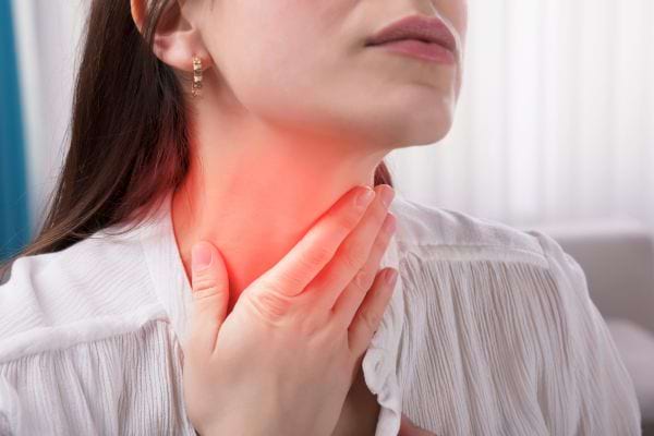 Une femme touche sa gorge irritée éclairée par une lumière rouge symbolisant la douleur.
