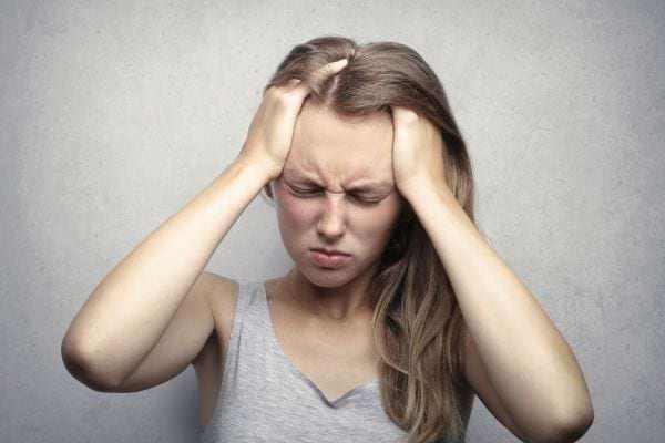Une femme se tient la tête avec les deux mains, les yeux fermés, exprimant la douleur d’un stress.