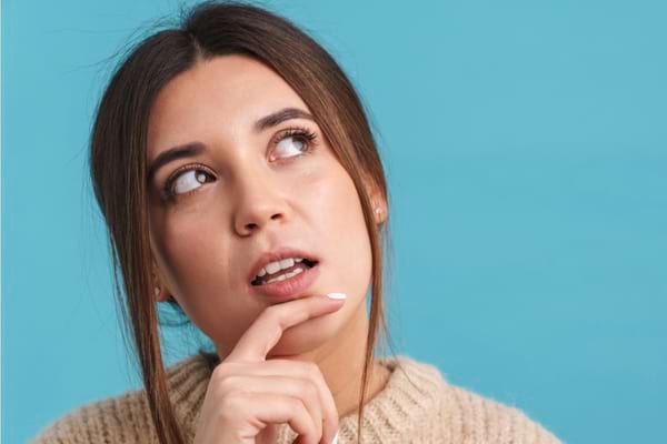 Femme brune pensive regardant vers le haut avec le doigt sur le menton.