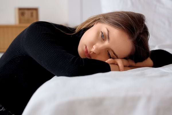 Une femme allongée sur un lit fixe le vide, l’air triste et fatigué.