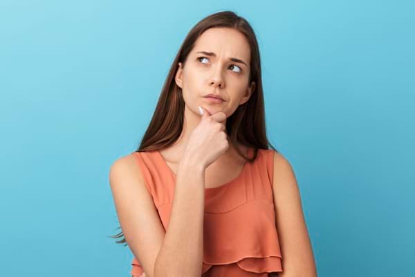 Jeune femme en robe orange pensant intensément avec la main sous le menton.