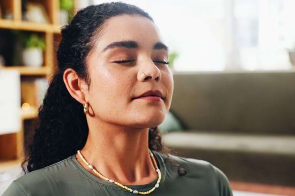 Une femme ferme les yeux et respire profondément dans une pièce au décor chaleureux.