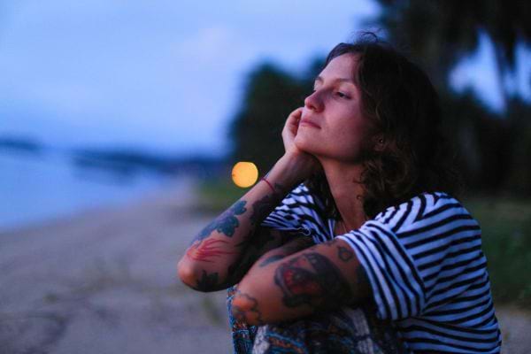 Une femme assise sur la plage regarde l’horizon, l’air songeuse et paisible.