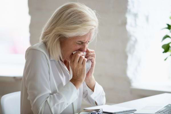 Femme âgée aux cheveux blancs pleurant avec un mouchoir devant son ordinateur.
