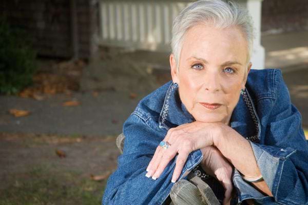 Portrait d’une femme senior aux cheveux courts gris, posant avec un regard sérieux.