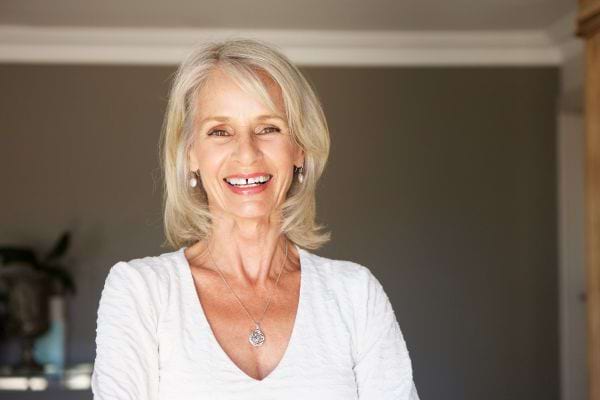 Portrait d’une femme âgée souriante aux cheveux gris, portant un haut blanc.