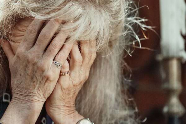 Femme âgée cachant son visage dans ses mains, exprimant la tristesse.