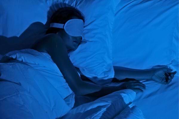 Femme dormant paisiblement dans un lit avec un masque de sommeil sous lumière bleue.