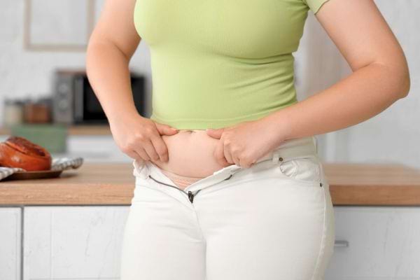 Femme en t-shirt vert tentant de fermer son pantalon trop serré à la taille.