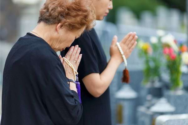 Deux femmes prient devant une tombe en tenant des chapelets.