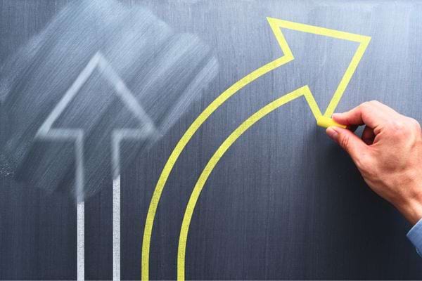 Une main trace une grande flèche jaune pointant vers le haut sur un tableau.