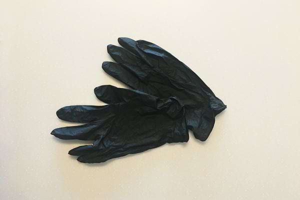 Paire de gants noirs jetables posée sur une surface claire, légèrement froissée.
