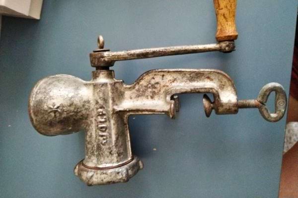 Hachoir à viande usé avec poignée en bois sur fond bleu.