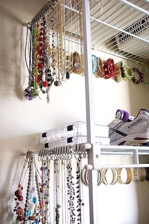 Des colliers, bracelets et boucles d'oreilles suspendus sur des étagères métalliques pour un rangement optimisé des bijoux.