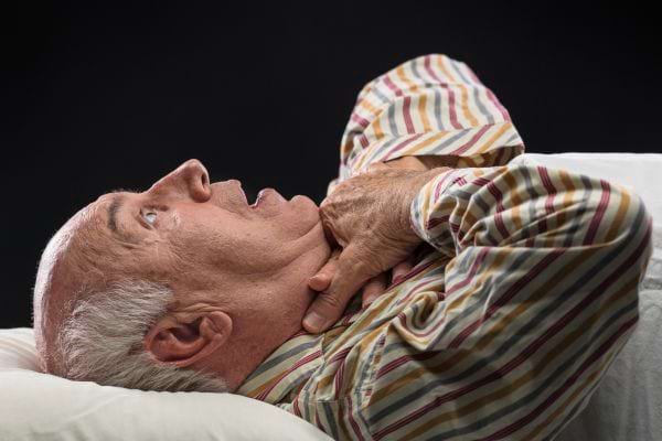 Un homme âgé allongé, main sur la gorge, semble éprouver une gêne respiratoire.