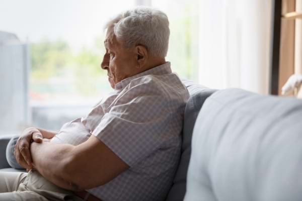 Un homme senior assis sur un canapé, les bras croisés, regardant dans le vide.