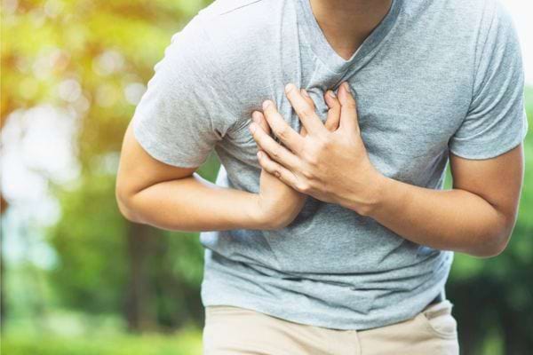 Un homme en t-shirt gris tient sa poitrine en grimaçant de douleur.