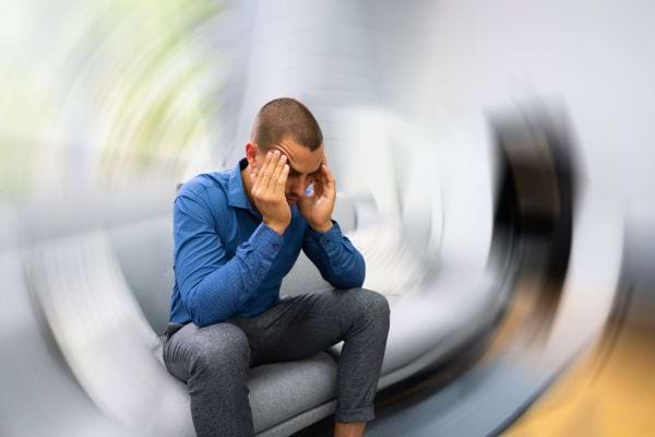 Un homme assis, en chemise bleue, se tient la tête avec un effet de vertige visuel.