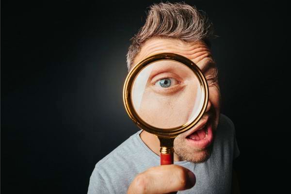 Un homme regarde à travers une loupe, agrandissant son œil avec une expression surprise.