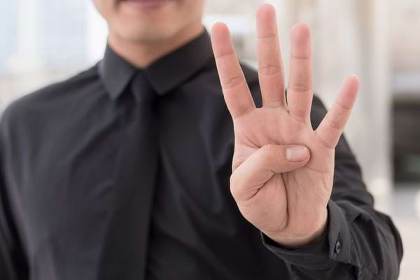 Homme en chemise noire montrant quatre doigts avec la main levée.