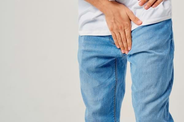 Un homme en jean tient son bas-ventre avec la main.