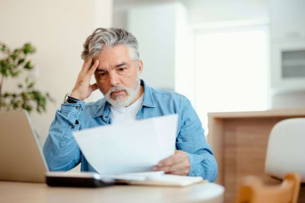 Un homme aux cheveux gris, inquiet, lit une facture devant son ordinateur.