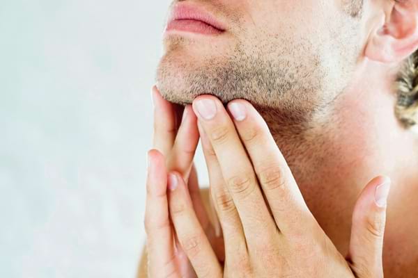 Homme touchant son menton en observant la pousse de sa barbe.