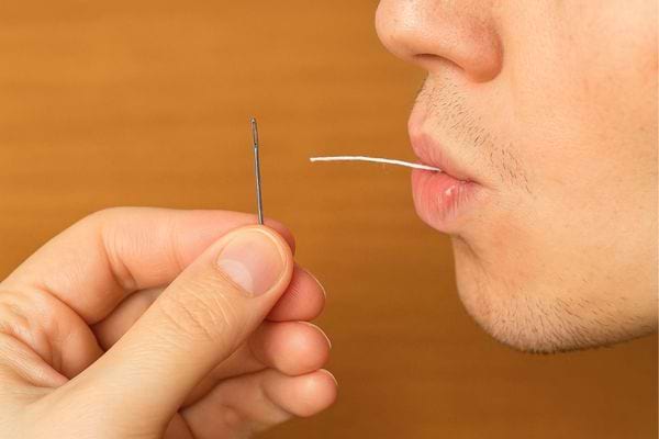 Un homme souffle sur le fil avant de l’enfiler dans l’aiguille.