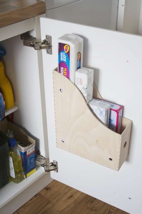 Un range-dossiers en bois est fixé à l’intérieur d’une porte de placard pour ranger rouleaux de papier aluminium et sacs plastiques.