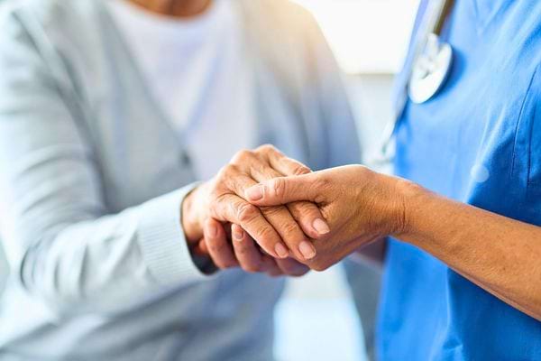 Une infirmière tient la main d’une personne âgée en signe de soutien.