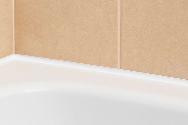 Joint blanc propre entre la baignoire et le carrelage beige.