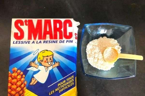 Boîte de lessive Saint Marc avec bol de poudre et cuillère en bois à côté.