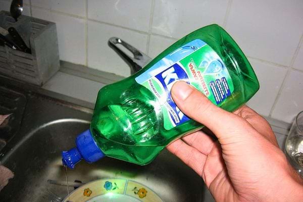 Main versant du liquide vaisselle vert au-dessus d’un évier, symbole du nettoyage quotidien.