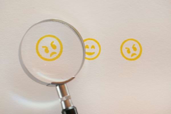 Une loupe met en avant un emoji en col&egrave;re parmi d&rsquo;autres visages jaunes.