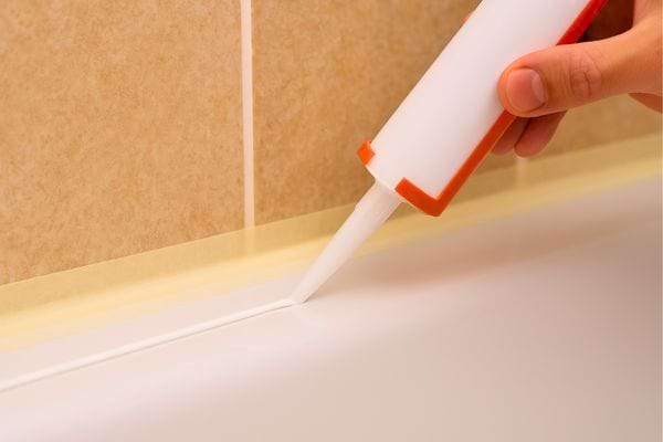 Main applique un nouveau joint de silicone le long de la baignoire.