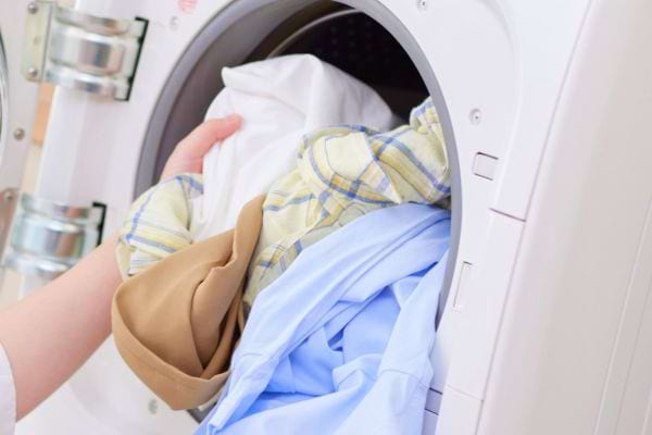 Main plaçant des vêtements dans une machine à laver.