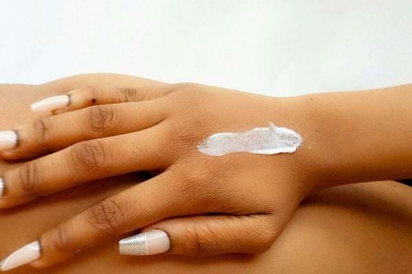Main avec crème blanche appliquée sur la peau.