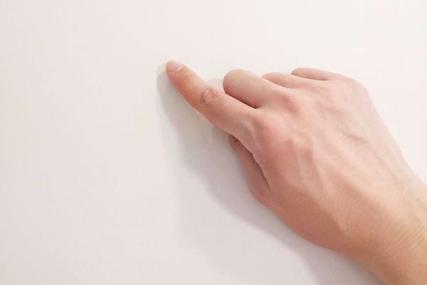 Main humaine pointant un mur blanc avec un doigt tendu.