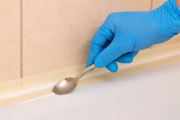 Main gantée lisse le joint avec le dos d’une cuillère.