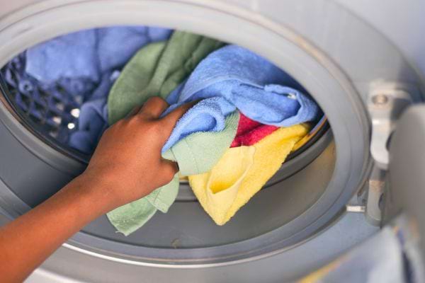 Main insérant du linge coloré dans un lave-linge.