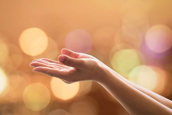 Une main tendue ouverte vers le ciel sur un fond doré lumineux.