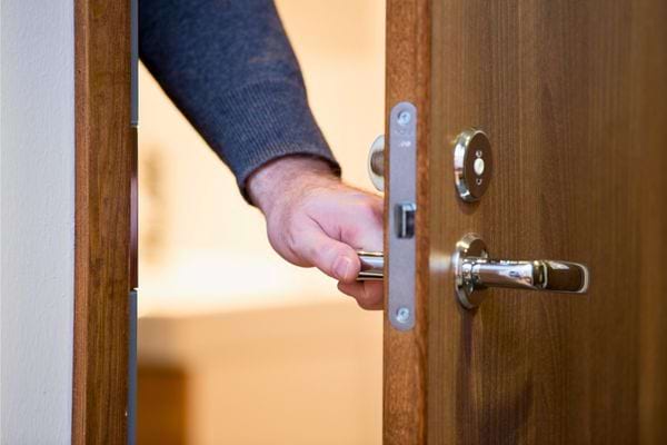 Main ouvrant une porte en bois.