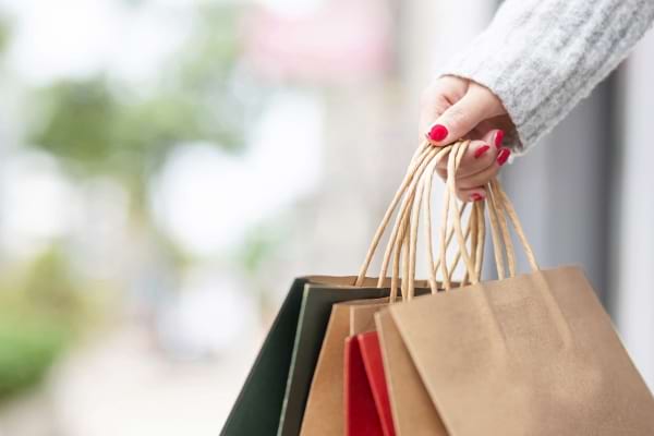 Une main tient plusieurs sacs de courses colorés dans la rue.