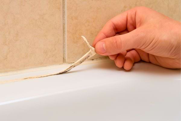 Main retire un vieux joint abîmé au bord de la baignoire.