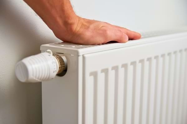 Main posée sur un radiateur blanc pour vérifier la chaleur.